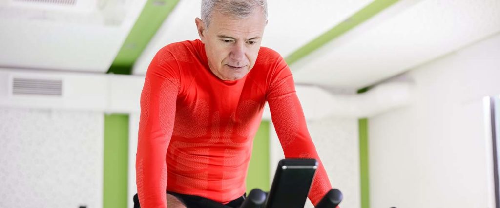 Man on an Indoor Bicycle Looking Down on His Phone