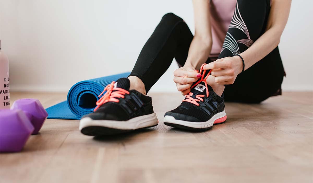 Woman tying her shoes next to a yoga mat and weights ready to workout. 