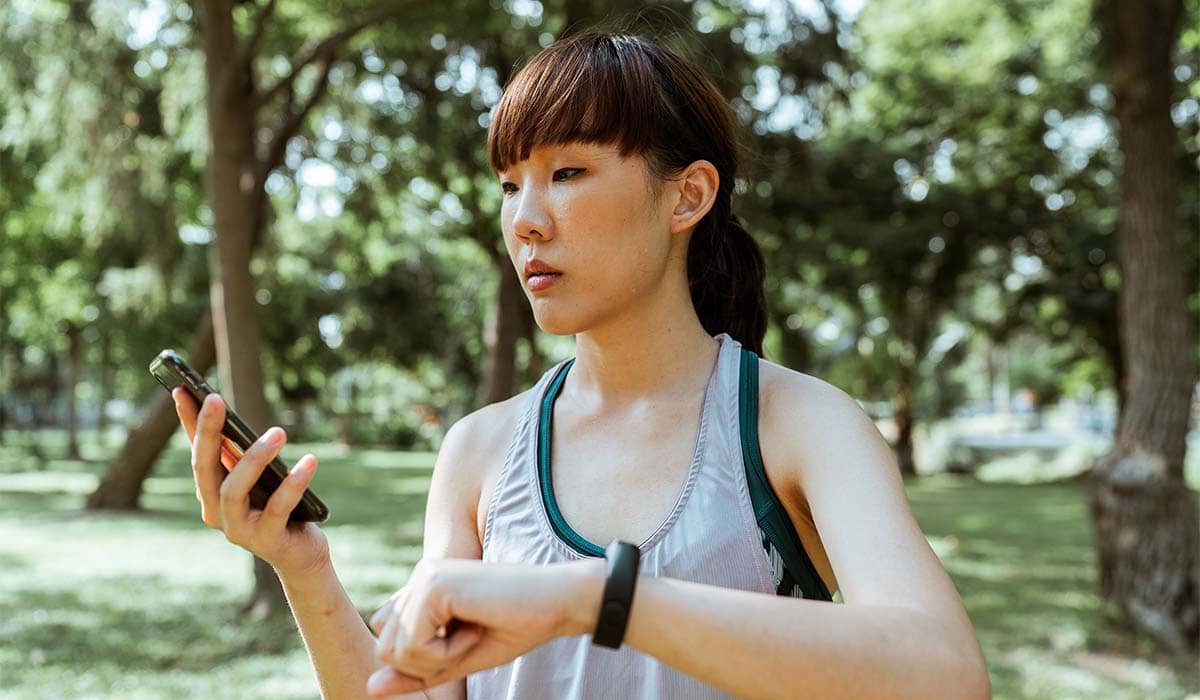 Woman looking at her phone and smart watch in a park.