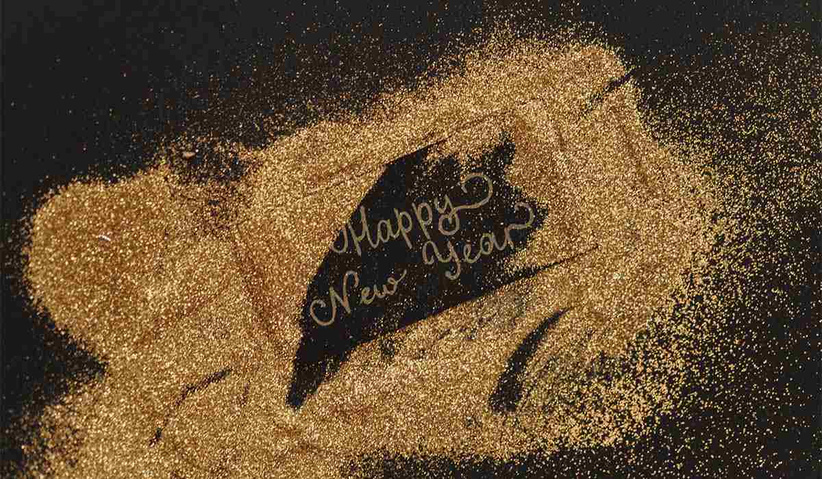 Gold written pen with glitter around a sign reading "Happy New Year"