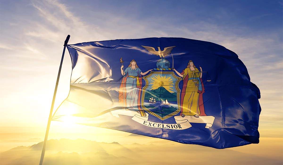 The New York State flag blowing in the wind during a sun set with the sun coming thru the flag. 
