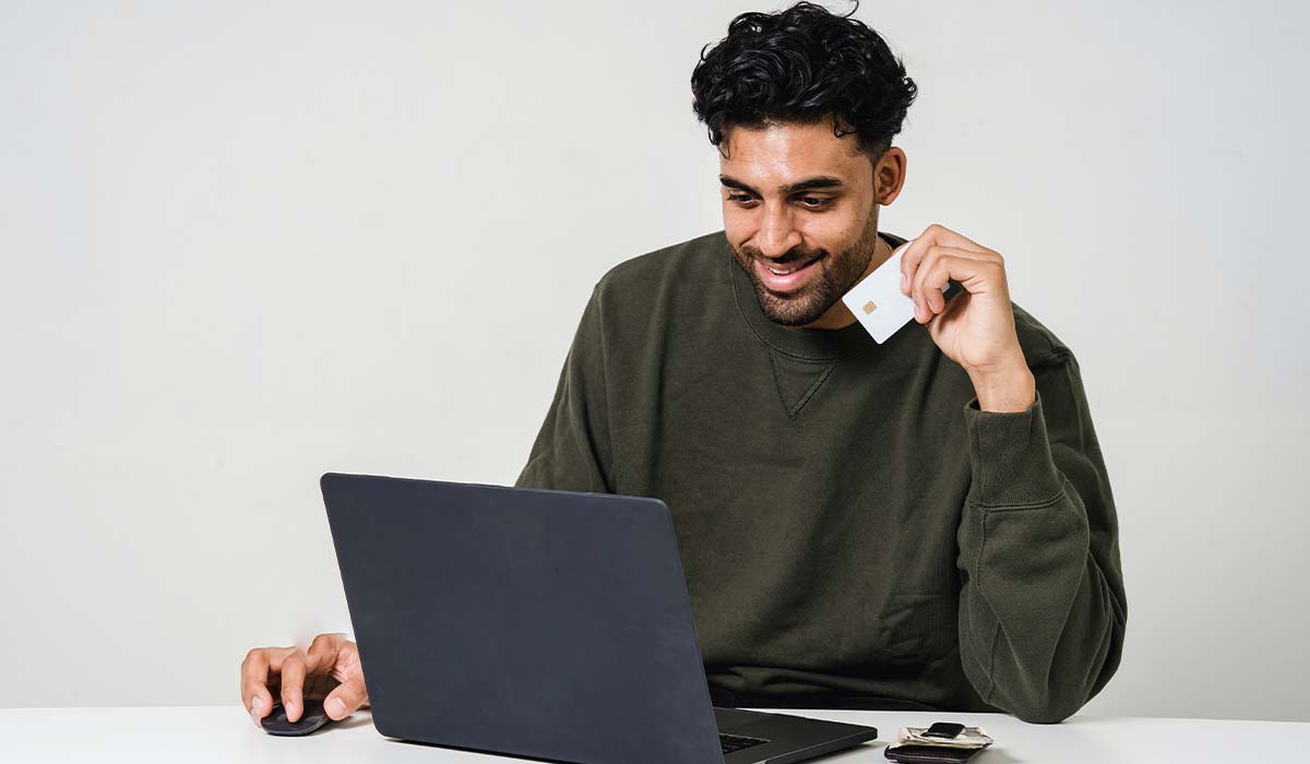 Man looking at his computer holding a credit card smiling. 