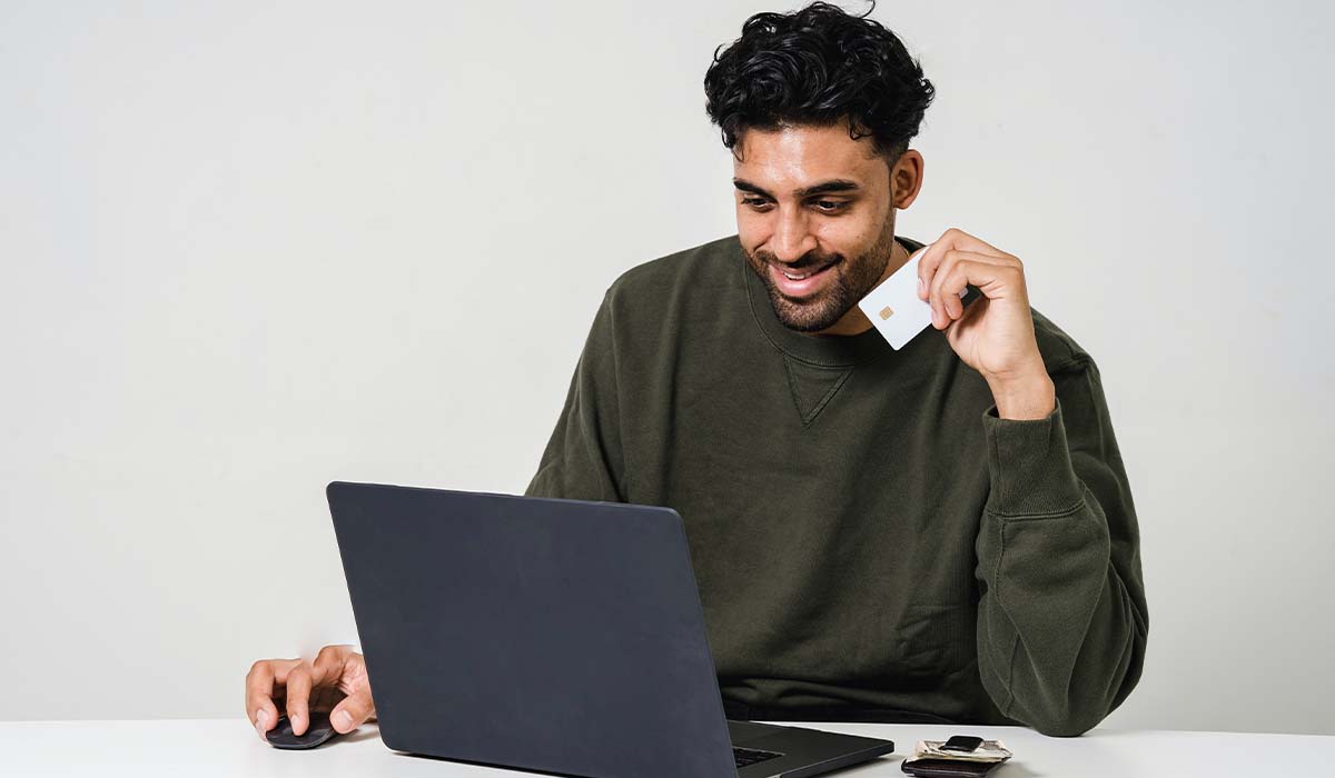 Man looking at his computer holding a credit card smiling.