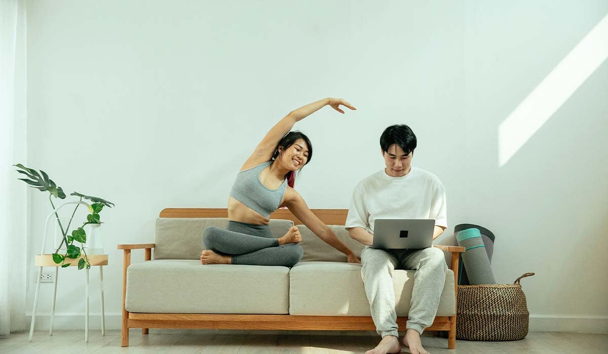 Couple on couch looking on their computer while stretching. 