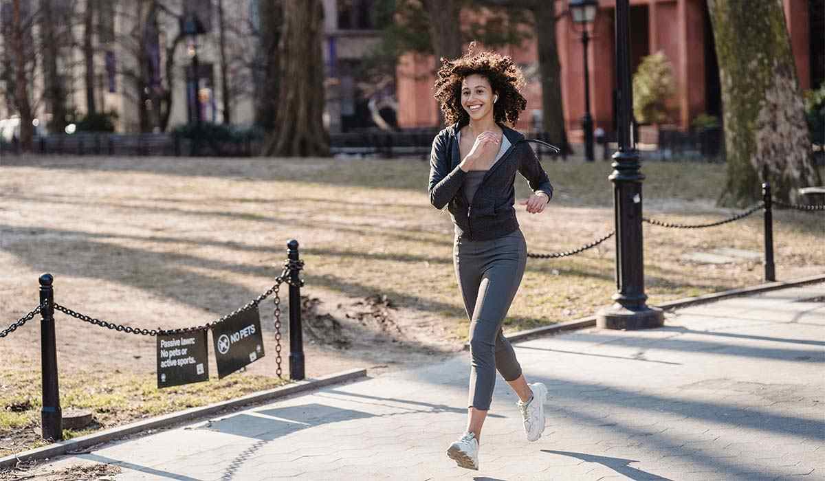 A woman running with a big smile in a park during the fall season. 