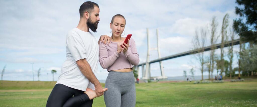 A couple stretching while looking at their phone in a park. 