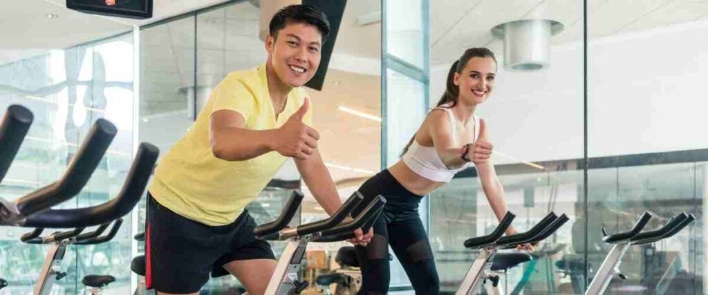 Two people cycling indoors giving the thumbs up!