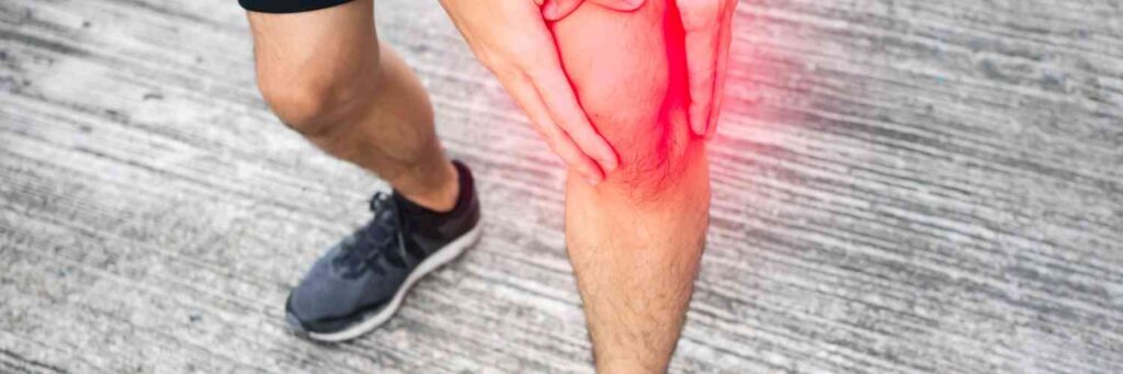 A man holding his knee in pain with a red area of where it hurts the most. 
