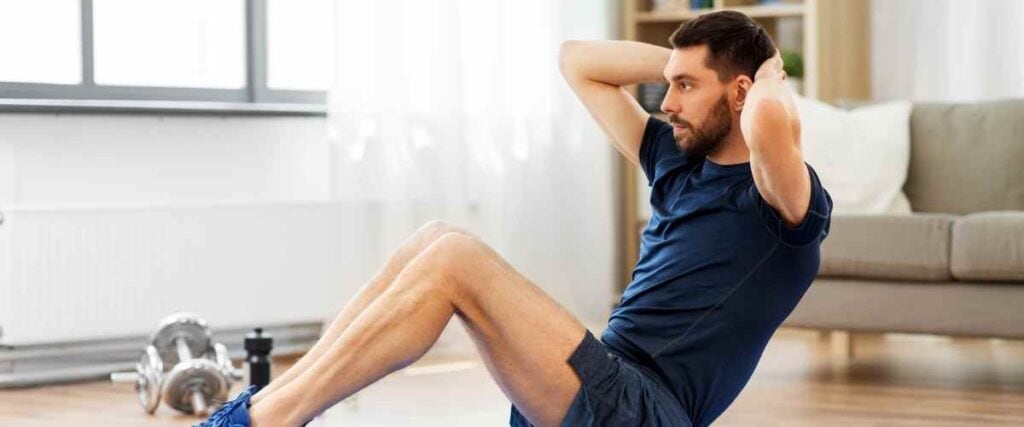 A man doing sit ups next to his couch at home.