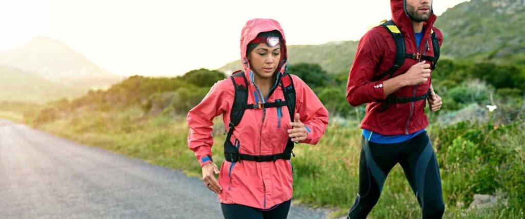 A couple running up a hill wearing backpack and rain jackets. 