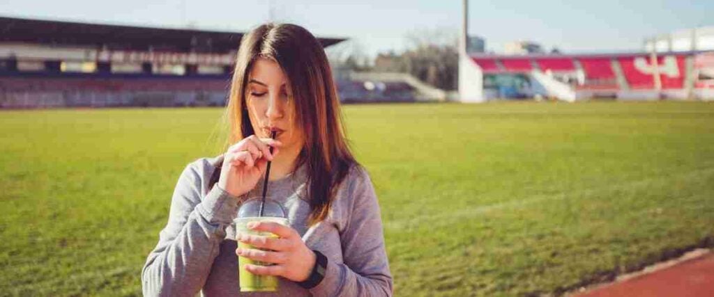 Woman drinking a green smoothie on running track. 