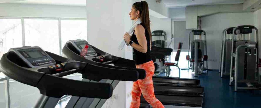 Woman on a treadmill walking with a towel behind her back. 