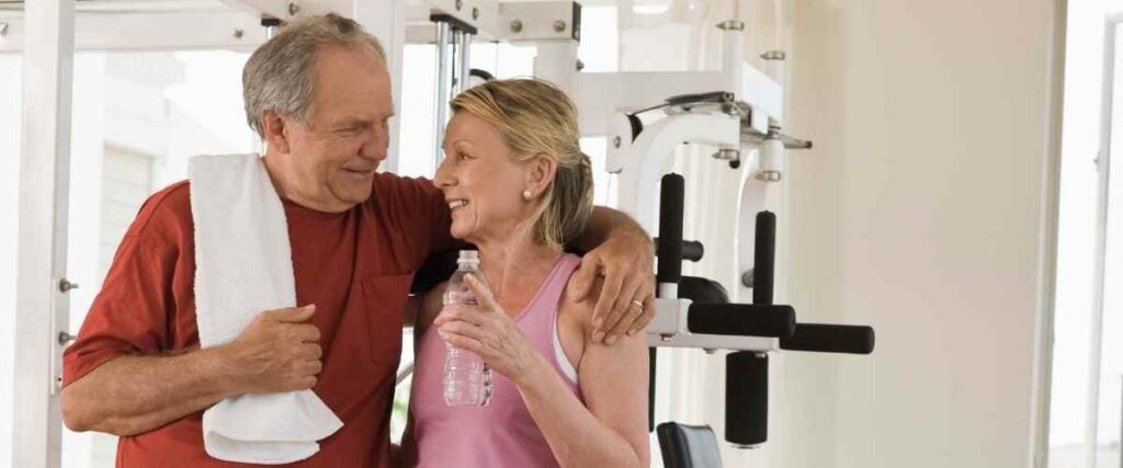 An older couple embracing after a workout at their home gym with a towel and water bottle.