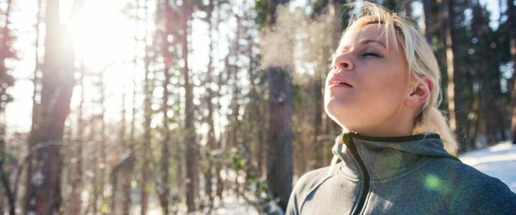 Woman eyes closed breathing in cold air in the forest. 