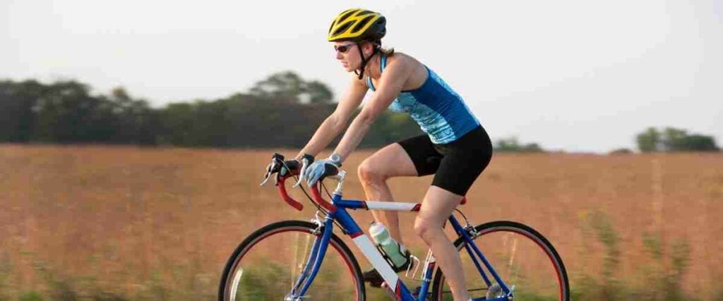 A female cyclists on the road next to a corn field. 