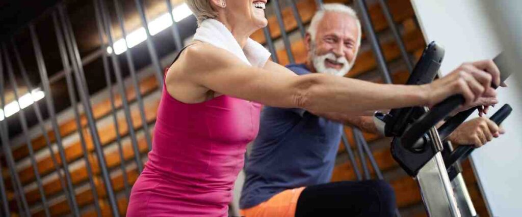 Older couple on indoor bikes smiling at each other.