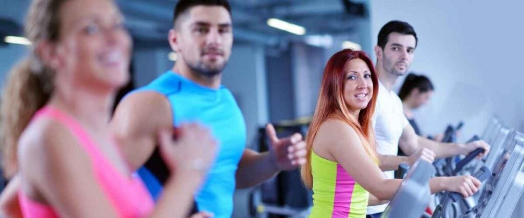A group of people at a gym, half on a treadmill and other half on the elliptical training. 
