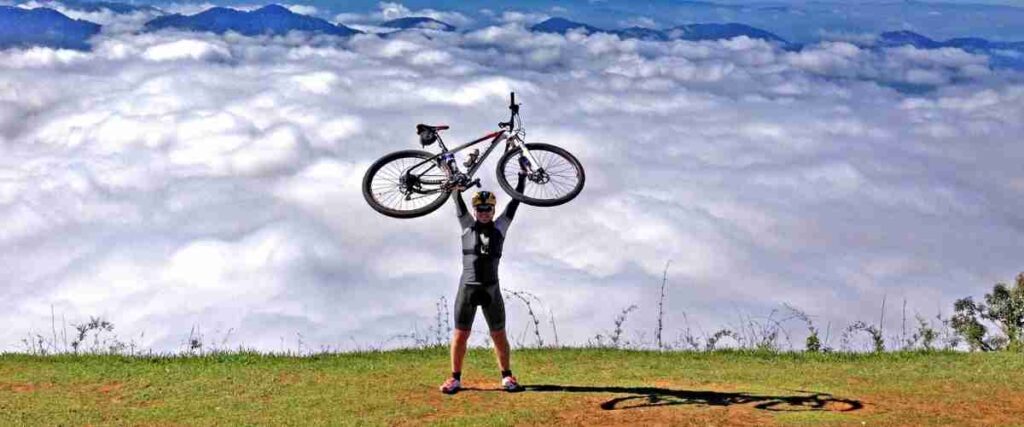 A male cyclists holding his bike over his head on top of a mountain. 