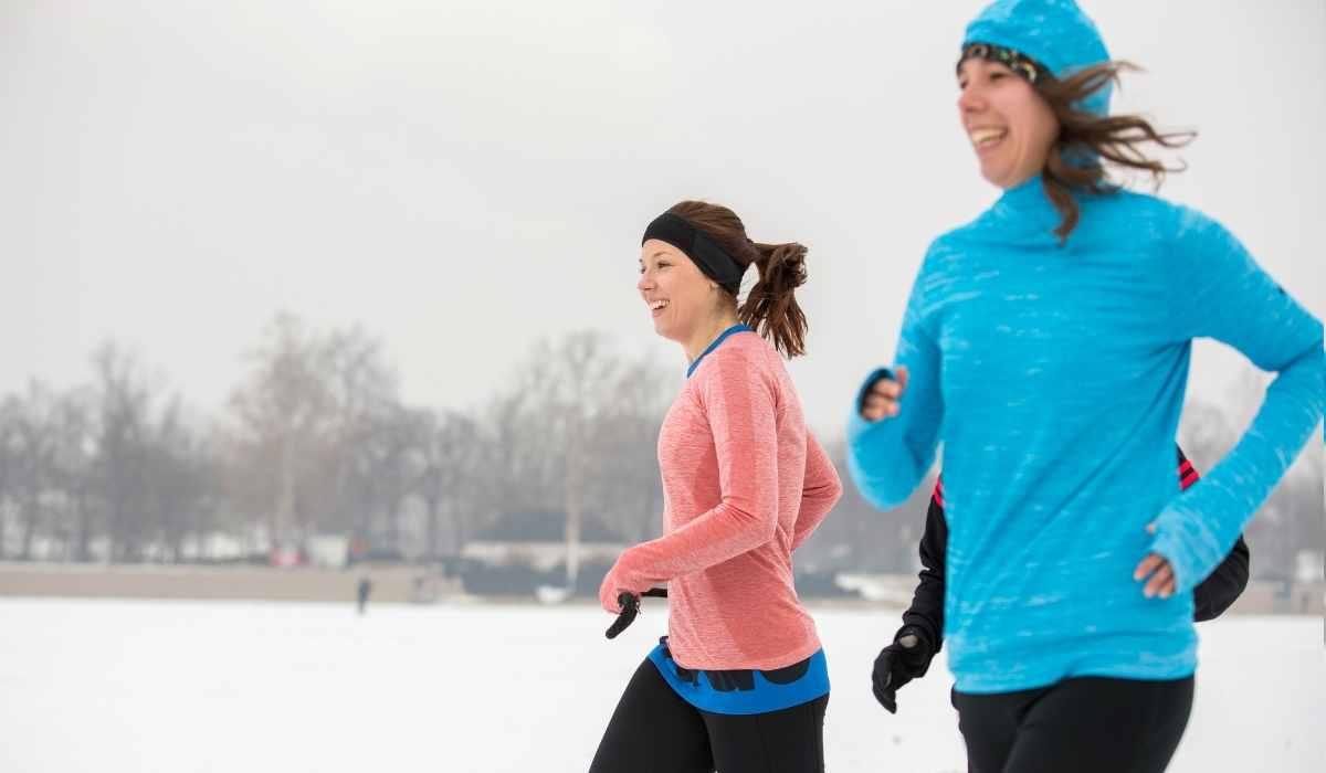 two women smiling while running in the snow in a park. 