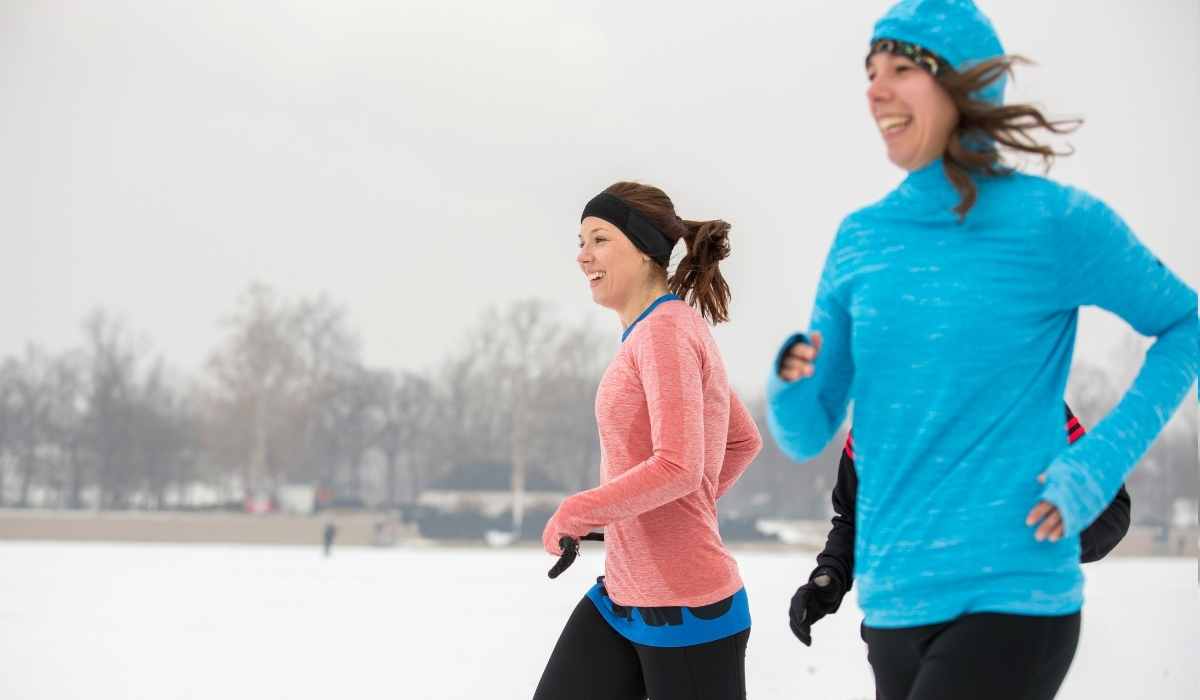 two women smiling while running in the snow in a park.