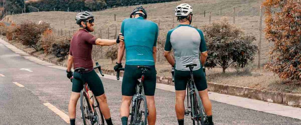 Group of male cyclists stopped at the side of the road smiling. 