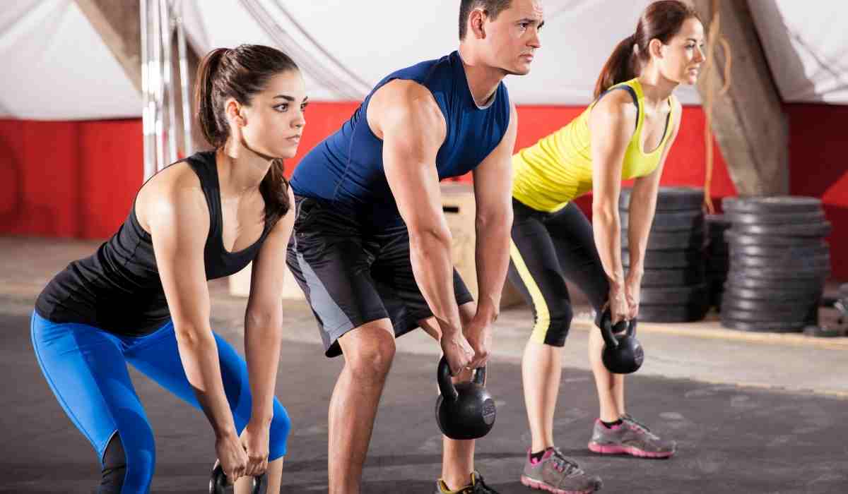 A group of men and women holding dumbbells during a squat looking at their instructor. 