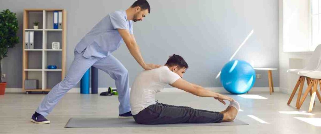 Two men, one a doctor pushing the back of another man on the floor to help stretch. 