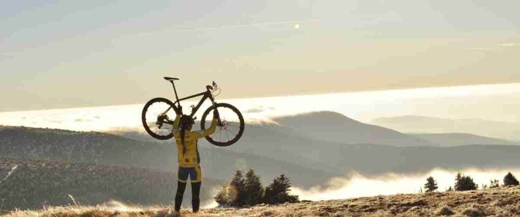 Woman holding her bike while on top of a mountain celebrating. 