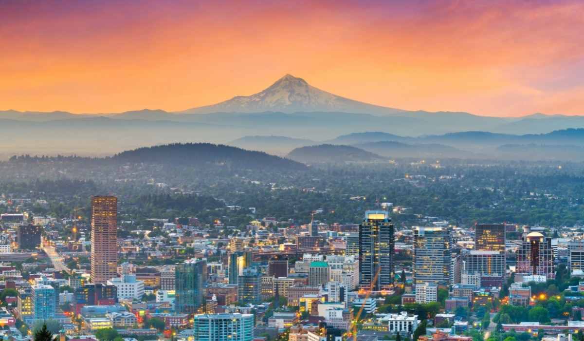 View of downtown Portland, OR with the view of the mountains in the background with an orange sky from the sunset. 