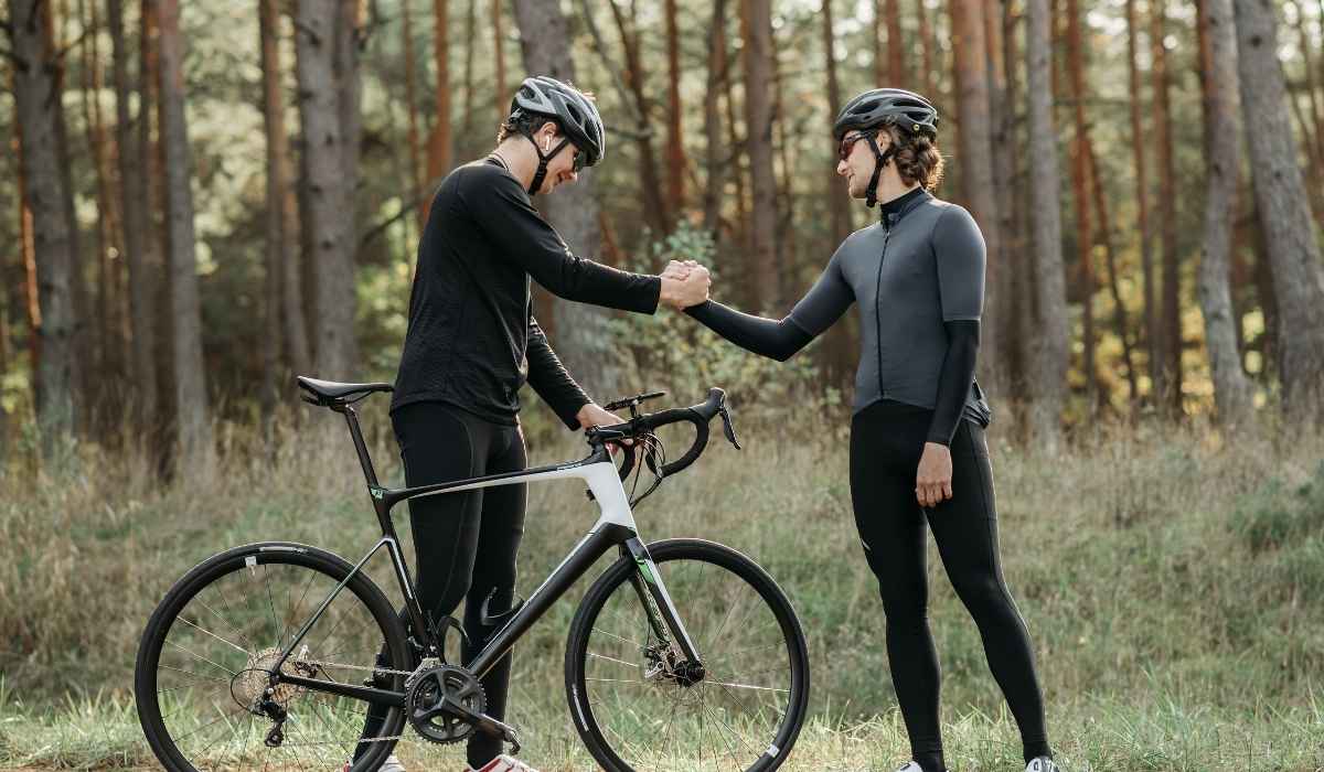 Two cyclists on the side of the road shaking each others hand. 