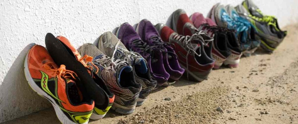 Group of dirty running shoes up against the wall.