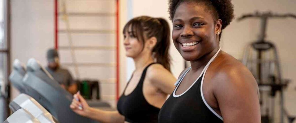 Two women on treadmill smiling to the left at the gym.
