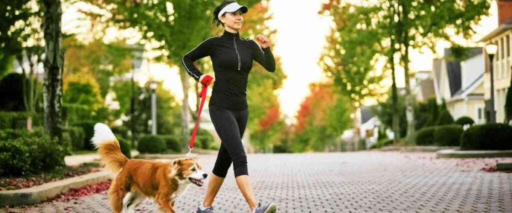 A female walking her dog mid walk with arms mid stride.