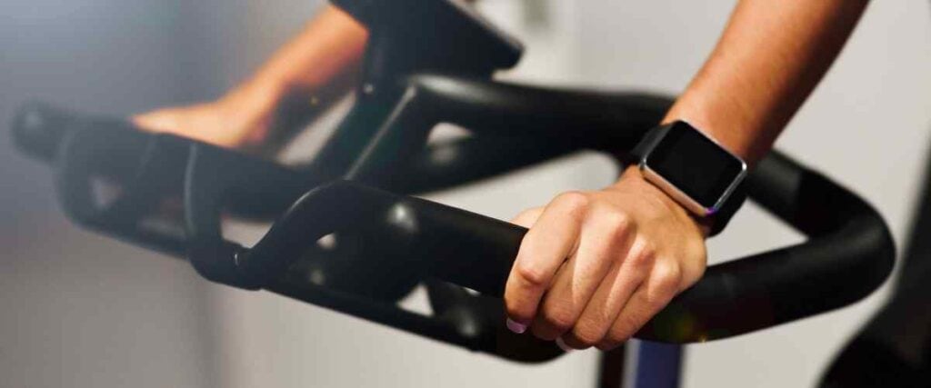 Close up of female hands on indoor bike with smart watch.