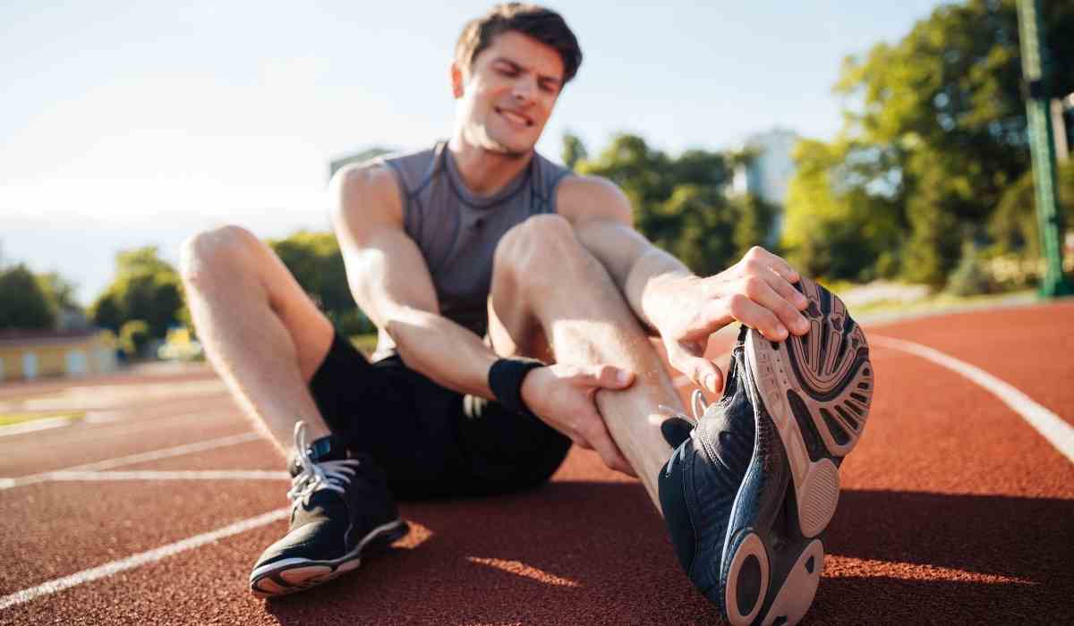 Man holding his leg due to a cramp on a track outside.