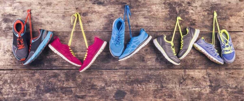 5 types of running shoes hanging up on the wall by the shoe laces.