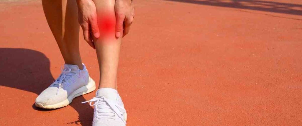 Female runner holding shins in pain with red area highlighting shins.