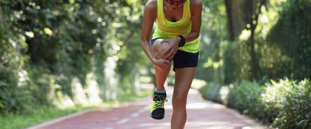 Female runner holding shins in pain. 