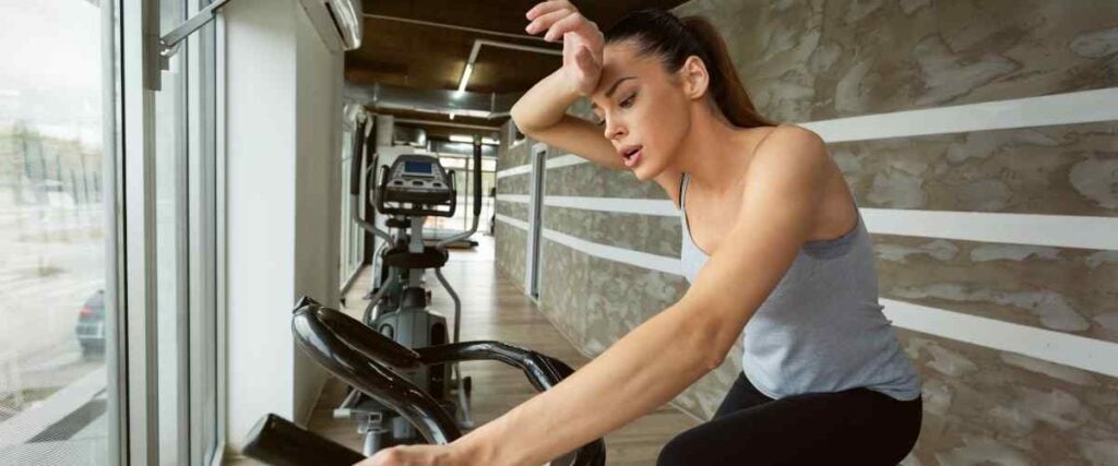 Female cyclist wiping sweat off forehead on indoor bike. 