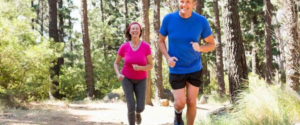 An older couple running in the forest with big smiles. 