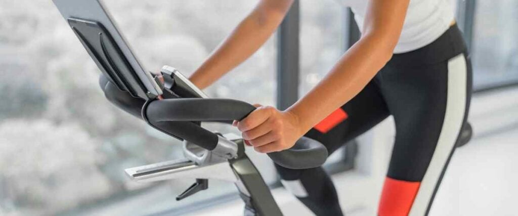 Close up on a woman riding an indoor bike with a emphasis on the center of the bike and its handles/saddle. 