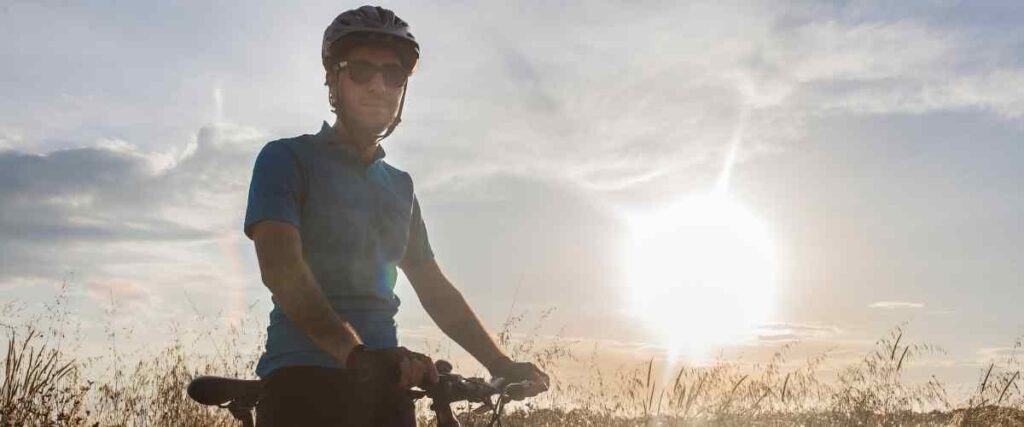 Male cyclist looking into camera on a field while the sun is rising. 