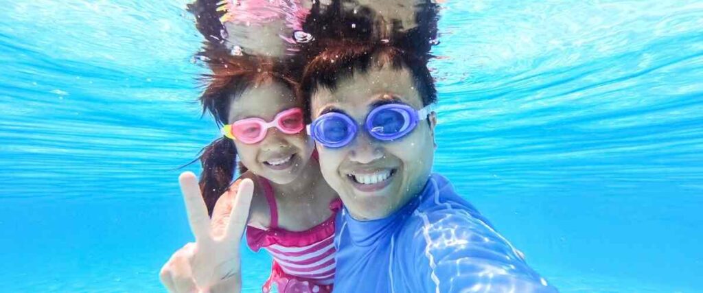A father and daughter under water in a pool smiling!