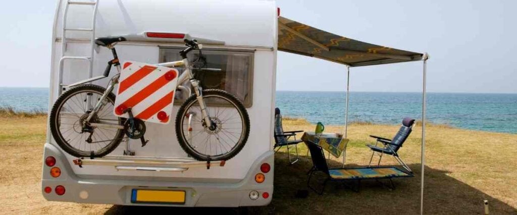 A camper parked next to the lake with a bike hitched to the back.