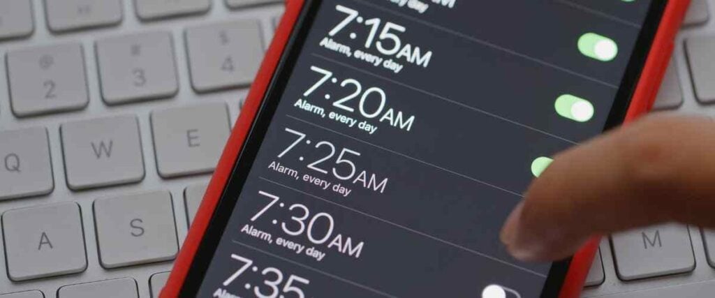 A phone with its alarm app open and 7 alarms activated to set for the early morning.