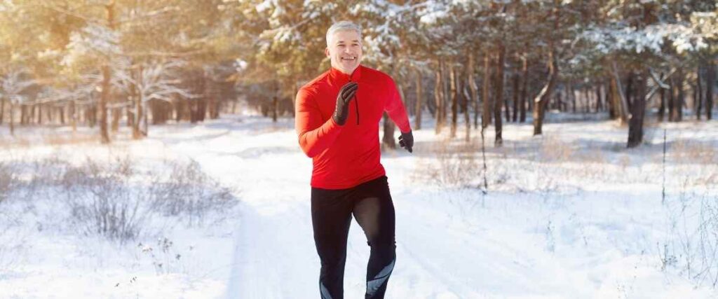 A man running on a snow trail from cars with a big smile. 