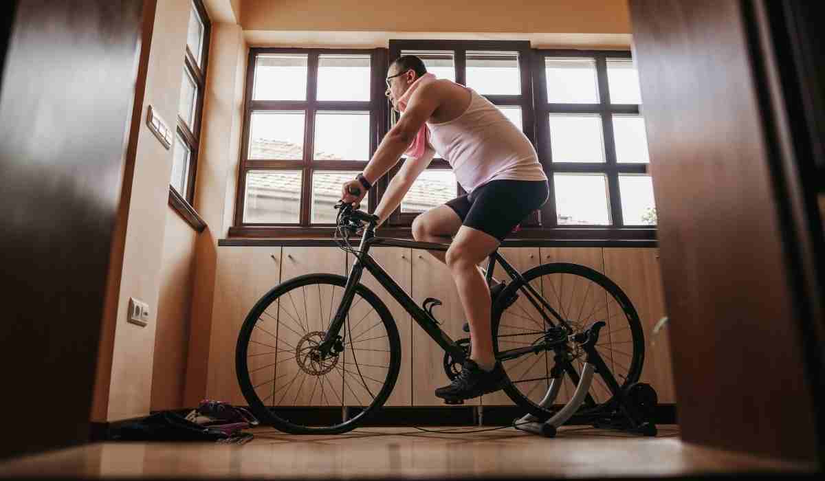 Male cyclists on his indoor trainer next to his windows in his living room.