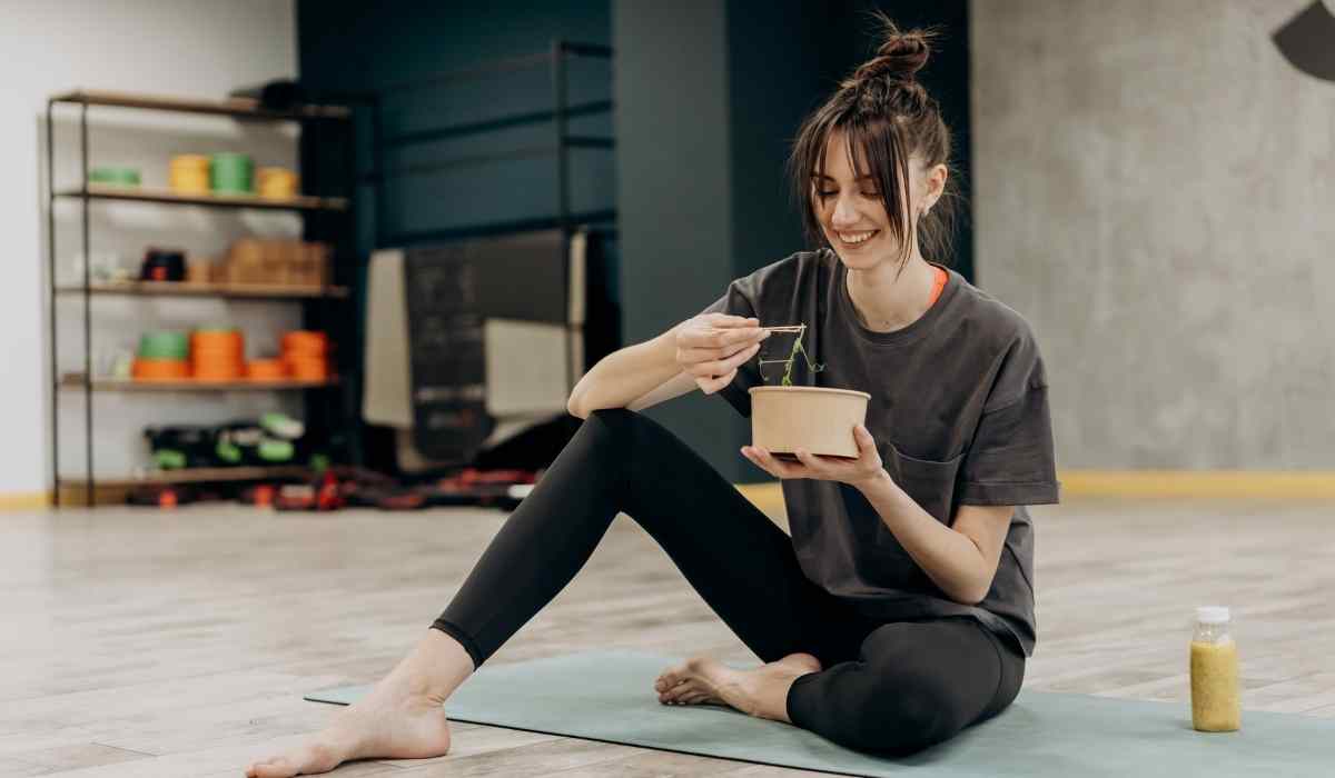 Woman eating noodles on her yoga mat in a gym. 