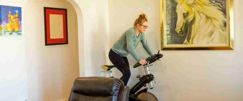 A woman doing HITT cycling on her indoor exercise bike in her living room next to a horse painting 