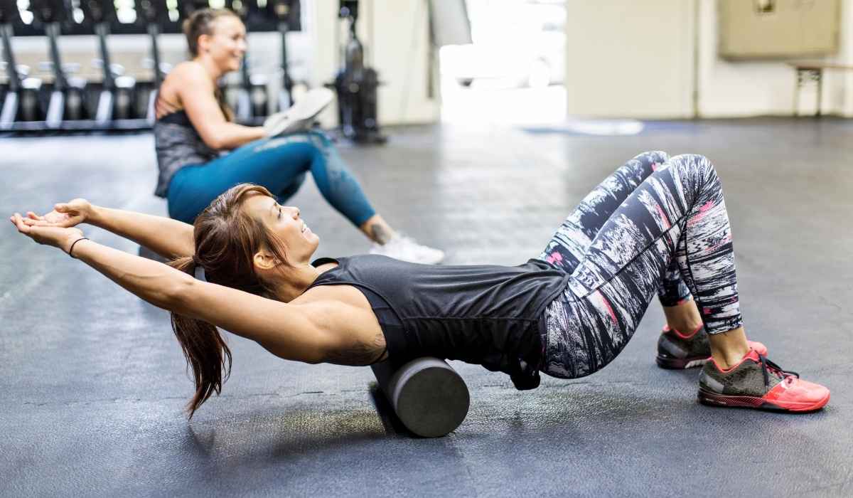 Woman at a gym foam rolling her back while screeched out. 